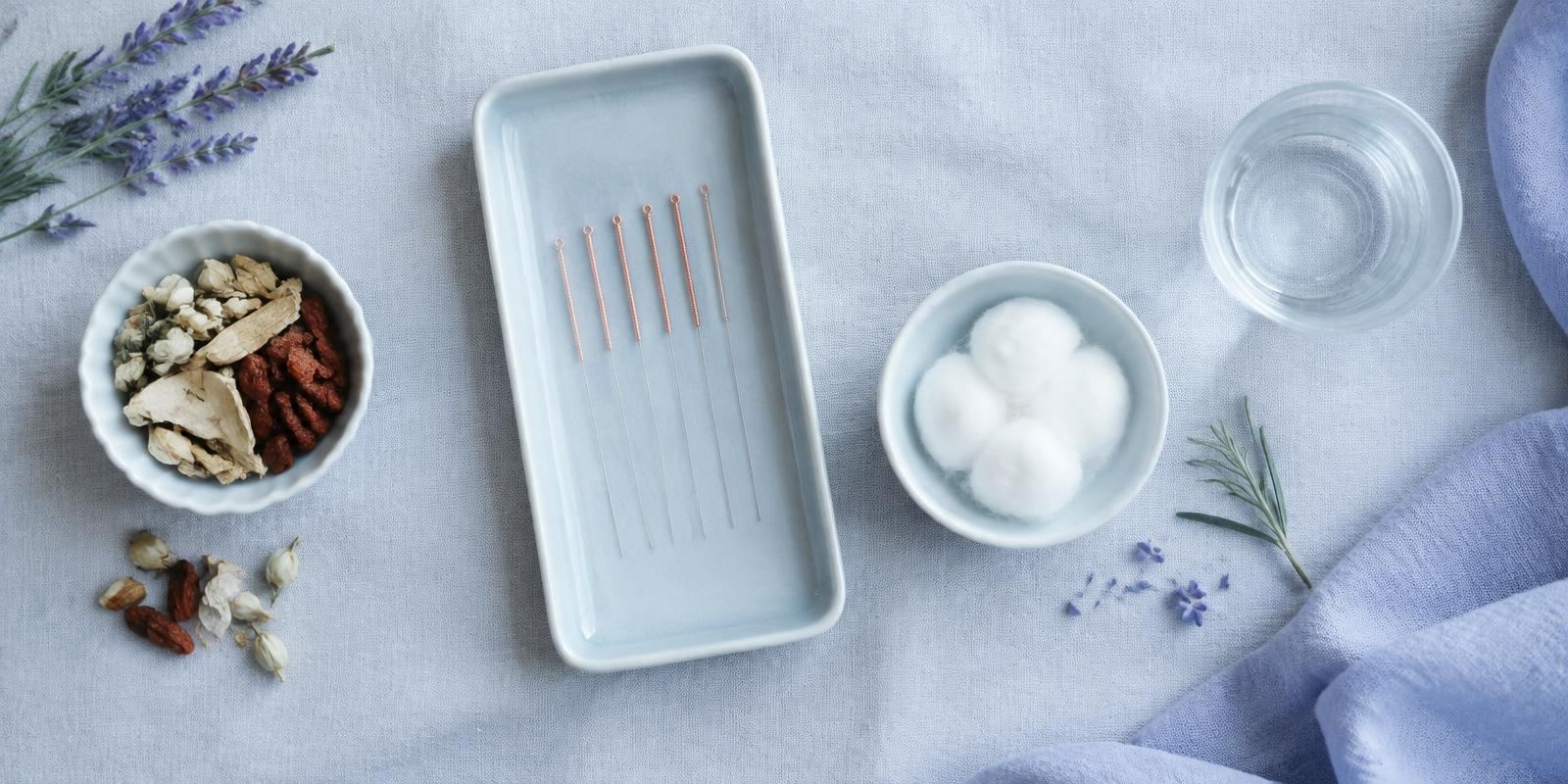 Sterile acupuncture needles, herbs and cotton laid out on linen